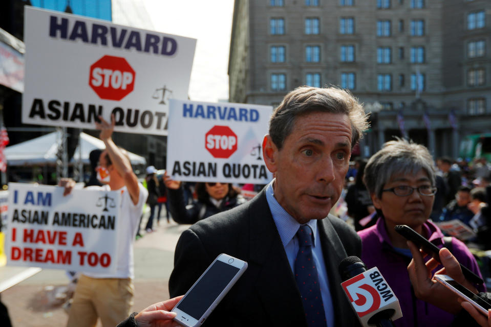 Edward Blum, founder of Students for Fair Admissions, speaks to reporters at an outdoor rally. Demonstrators behind him hold signs reading: Harvard stop Asian quota.