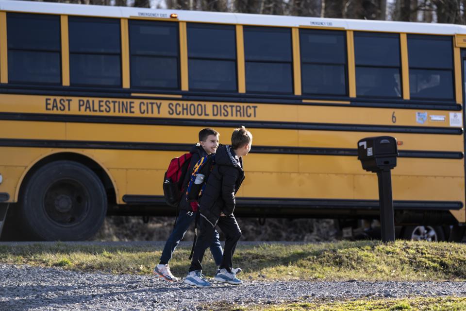Noah Conard, 10, left, and his brother Jagger, Conard, 9, walk past the school bus that dropped them off in East Palestine, Ohio, Tuesday, March 7, 2023. Jessica Conard wonders after the train derailment if her kids will ever be able to fish in the pond separating their property from the railroad tracks. Or play at the park where the chemicals are being removed from a stream. Can they remain in the town where "generations upon generations" of family have lived? (AP Photo/Matt Rourke)