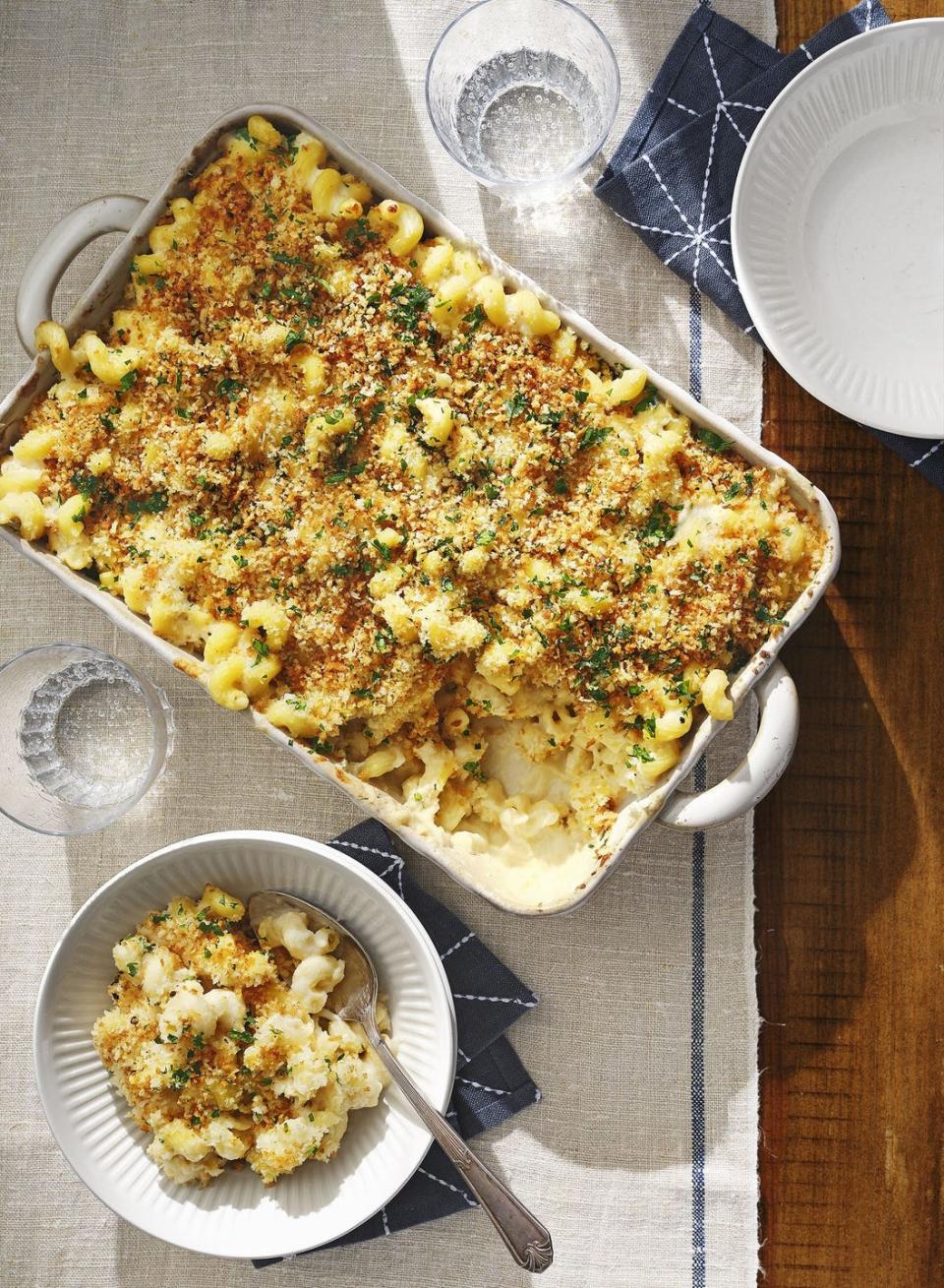 cauliflower mac and cheese in a white rectangle baking dish with some scooped into a white bowl with a spoon next to it