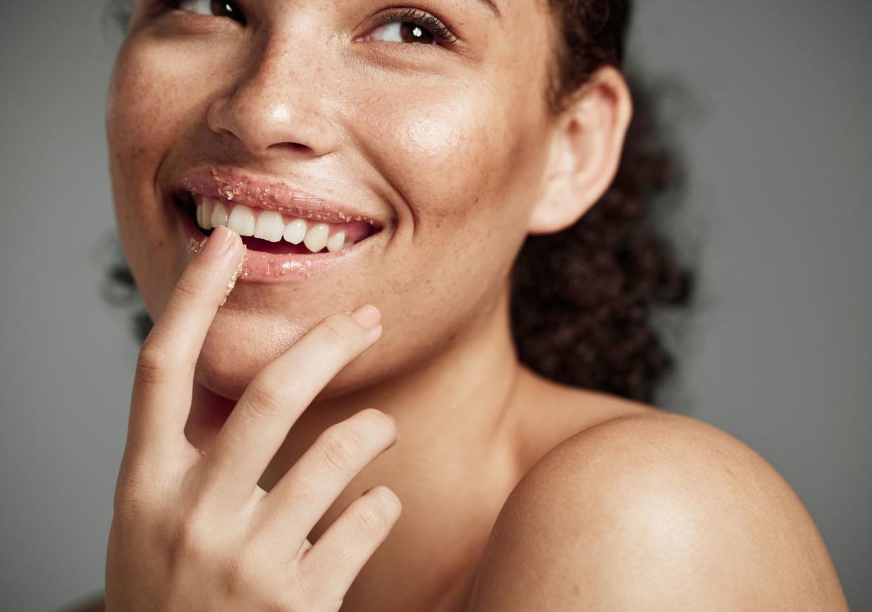 woman, sugar scrub and lips with smile for skincare, makeup or cosmetics against a grey studio background happy female smiling in happiness for facial cosmetic, lip dermatology or mouth exfoliation