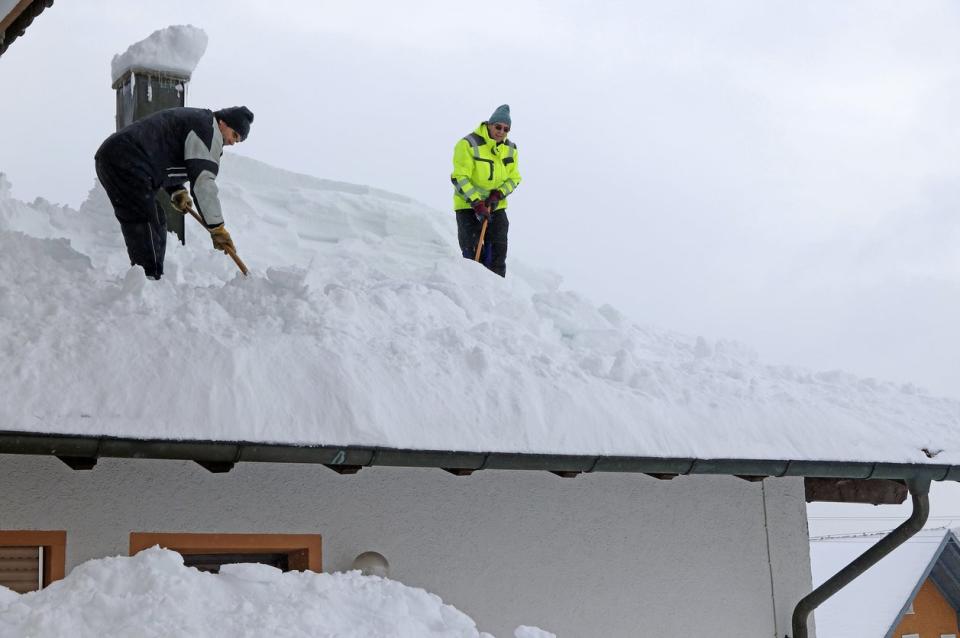 Two workers remove snow from a roof.