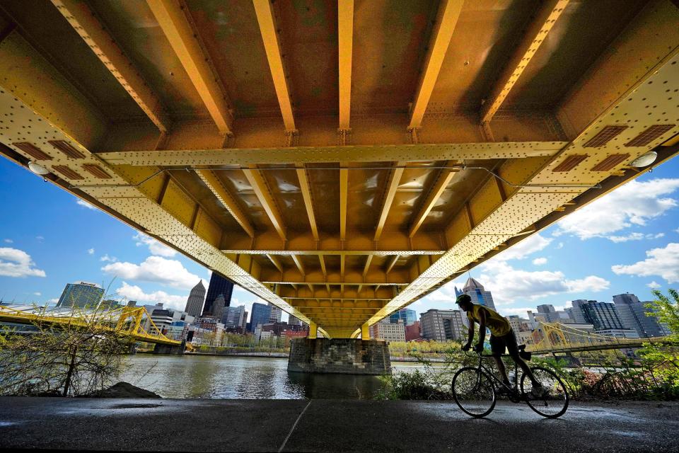 A cyclist rides on the North Shore Riverfront trail under the recently refurbished Andy Warhol bridge in downtown Pittsburgh, Monday, April 19, 2021.