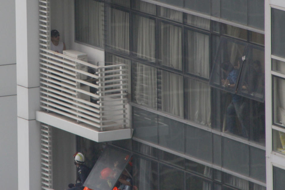 A man in a blue shirt seen speaking to the man on the ledge as SCDF officers make rescue reparations from a floor below. (PHOTO: Dhany Osman / Yahoo News Singapore)