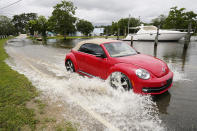 A passenger car drives through a road flooded by the Tchoutacabouffa River along Cedar Lake Road in Biloxi, Miss., Saturday, June 19, 2021, as water from Tropical Storm Claudette begins to recede. The storm brought much evening and early morning rain and flooded various communities along the Mississippi Gulf Coast. (AP Photo/Rogelio V. Solis)