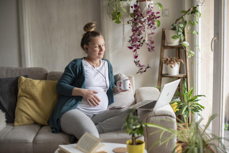 pregnant woman on the couch with headphones in and mug in hand