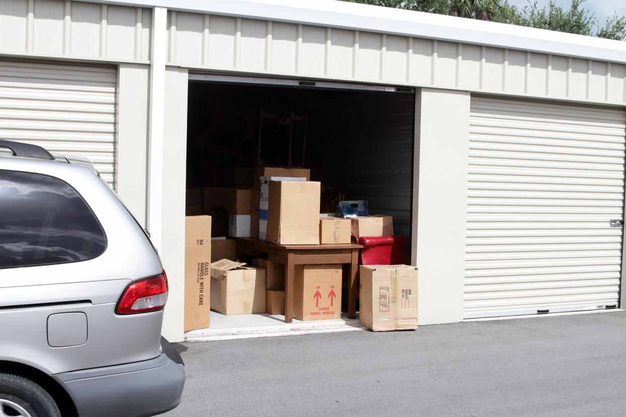 an open self storage unit, filled with boxes, with a van parked next to it