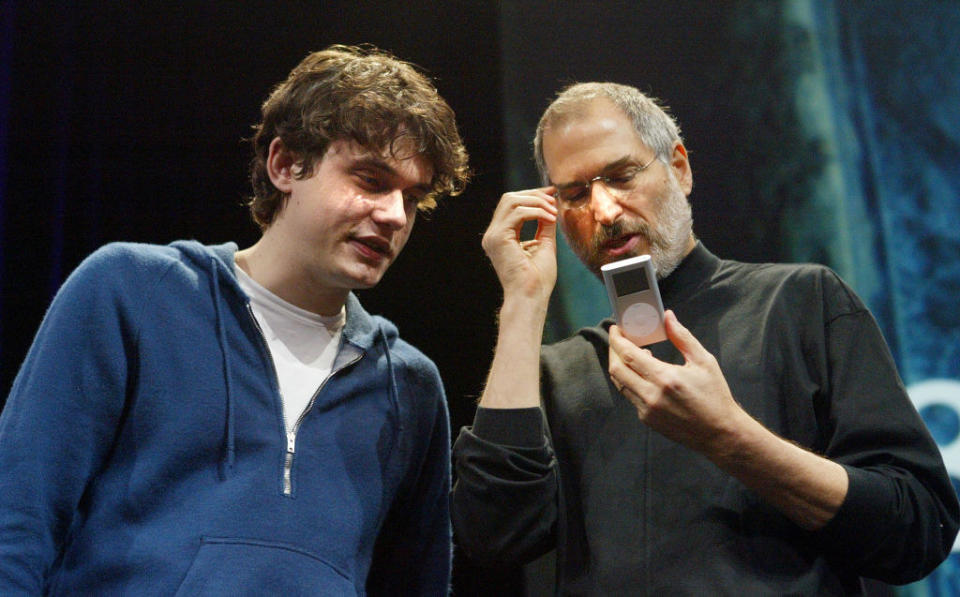 John Mayer in a hoodie standing next to Steve Jobs and looking at the iPod he's holding