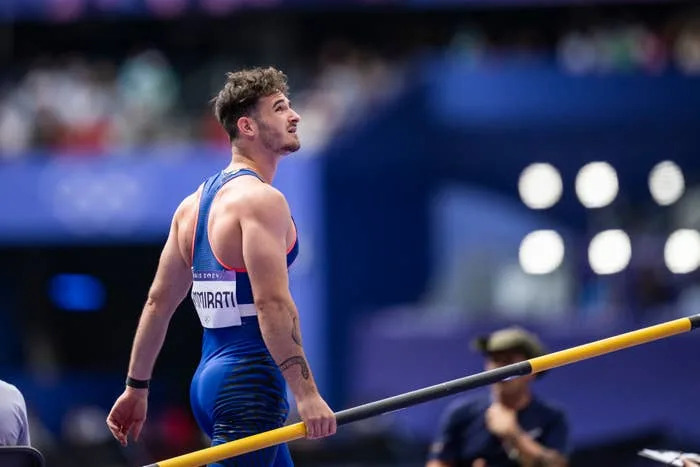 An athlete is seen on a track field holding a pole vault