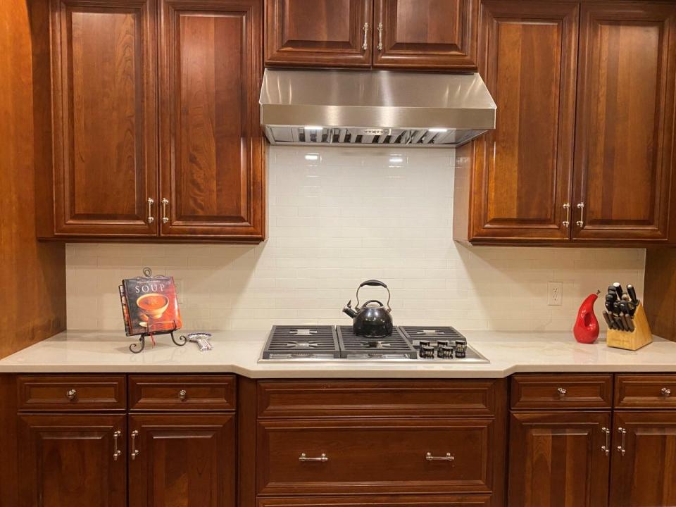 AFTER: A cream-colored, glossy, subway-tile backsplash along with new counters, a new cooktop and range hood, and updated cabinet hardware help to modernize a kitchen that had outlived its prime.