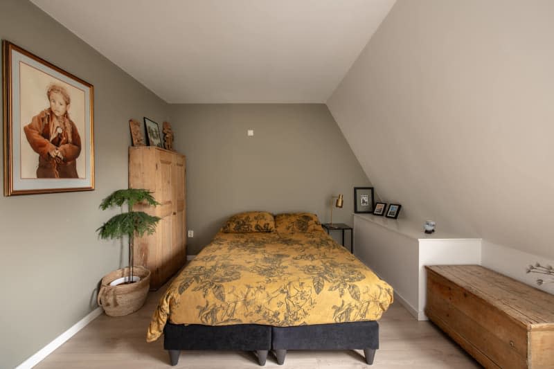 Angled ceiling, built in wall shelf, low wood trunk, yellow leaf pattern bedding, portrait on wall, light natural wood wardrobe