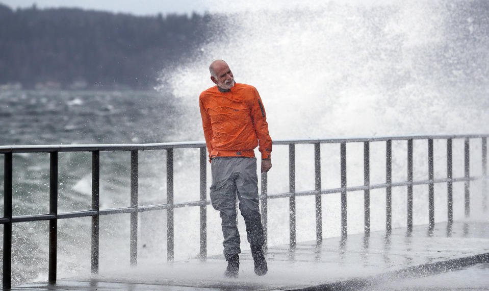 Bender, who goes by a singular name, leans against the wind as waves crash against a seawall next to him at high tide during a windstorm Thursday, Dec. 20, 2018, in Seattle. More than 140,000 households and businesses lost power Thursday as strong winds toppled trees, closed roads and even trapped a trampoline between power lines in western Washington. A high wind warning remained in effect for much of area into Thursday evening, with gusts up to 60 miles an hour recorded earlier in the day. (AP Photo/Elaine Thompson)