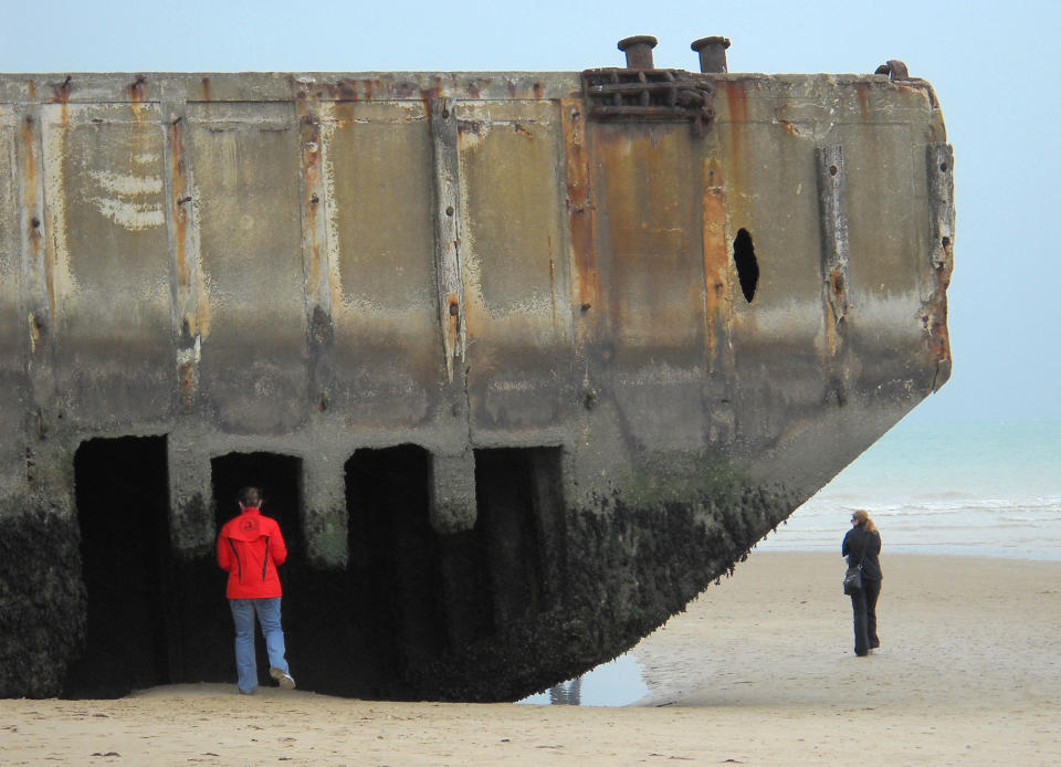 This Oct. 13, 2013 photo shows a visitor inspecting the remains of an artificial harbor used by Allied forces during World War II on the sand at Arromanches, France. Arromanches is one of several beaches on the coast of Normandy likely to see an influx of tourists for the 70th anniversary of D-Day on June 6, 2014. (AP Photo/Kathy Matheson)