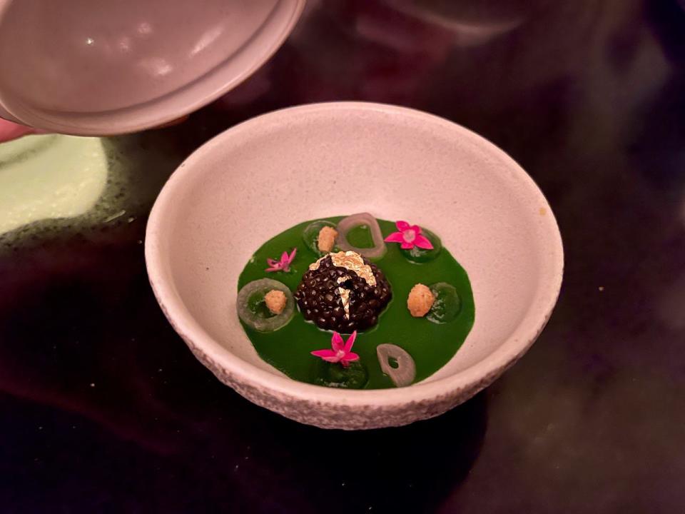 A white bowl with a green sauce and caviar topped with gold leaf.