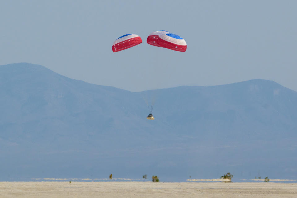 spacecraft under parachutes lands in front of the mountains, in a desert