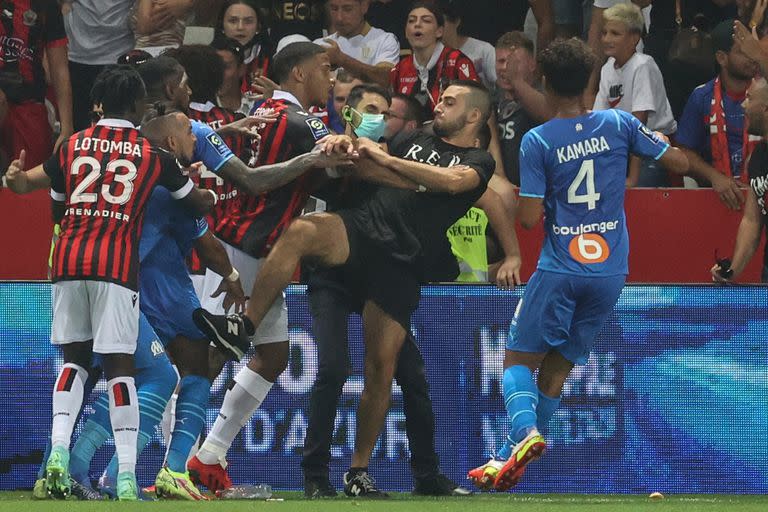 Jugadores de OGC Nice (camiseta roja y negra) y Olympique de Marseille (camiseta azul) detienen a un fan que invade el campo durante el partido de fútbol francés L1 entre OGC Nice y Olympique de Marseille (OM) en el estadio Allianz Riviera en Niza, en el sur de Francia. el 22 de agosto de 2021.