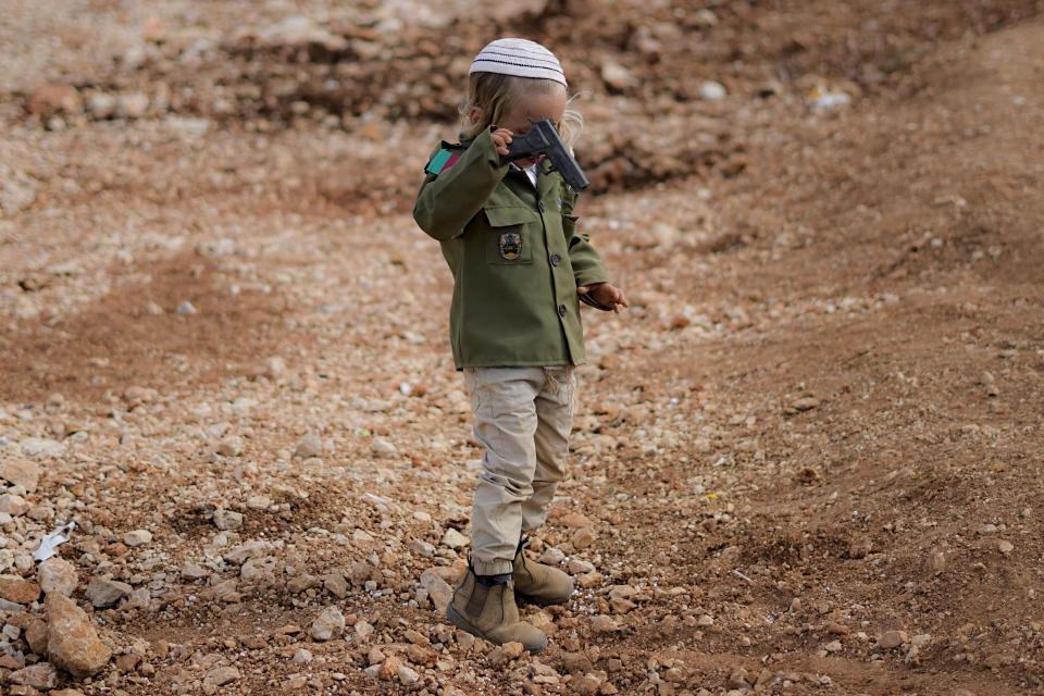 Yossef, a Jewish settler boy, wears costumes as an Israeli soldier, as he plays with a toy gun during the Jewish festival of Purim, next to Tapuach junction checkpoint, not far from the Palestinians city of Nablus, Tuesday March 7, 2023. The Jewish holiday of Purim commemorates the Jews salvation from genocide in ancient Persia, as recounted in the Book of Esther. (AP Photo/Ariel Schalit)