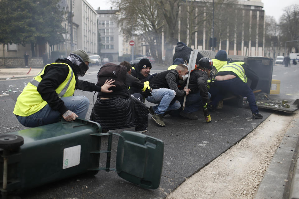 Yellow vest demonstrators take cover during clashes with French riot police during a demonstration in Bourges, central France, Saturday, Jan. 12, 2019. Paris brought in armored vehicles and the central French city of Bourges shuttered shops to brace for new yellow vest protests. The movement is seeking new arenas and new momentum for its weekly demonstrations. Authorities deployed 80,000 security forces nationwide for a ninth straight weekend of anti-government protests. (AP Photo/Rafael Yaghobzadeh)
