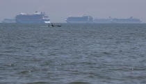 A boat passes by cruise ships carrying Filipino and foreign seafarers anchored at Manila's bay, Philippines, Thursday, May 7, 2020, as they wait clearance from the Bureau of Quarantine to dock at the port. Tens of thousands of workers have returned by plane and ships as the pandemic, lockdowns and economic downturns decimated jobs worldwide in a major blow to the Philippines, a leading source of global labor. (AP Photo/Aaron Favila)