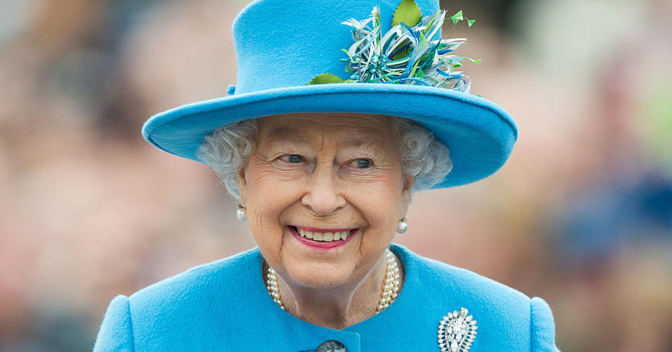 The Queen wearing a blue jacket and blue hat while smiling