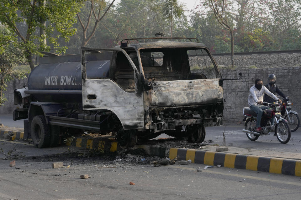 Motorcyclists drive past a burnt truck near the site of clashes between supporters of former Prime Minister Imran Khan and riot police officers, in Lahore, Pakistan, Wednesday, March 15, 2023. Clashes between Pakistan's police and supporters of Khan persisted outside his home in the eastern city of Lahore on Wednesday, a day after officers went to arrest him for failing to appear in court on graft charges. (AP Photo/K.M. Chaudary)