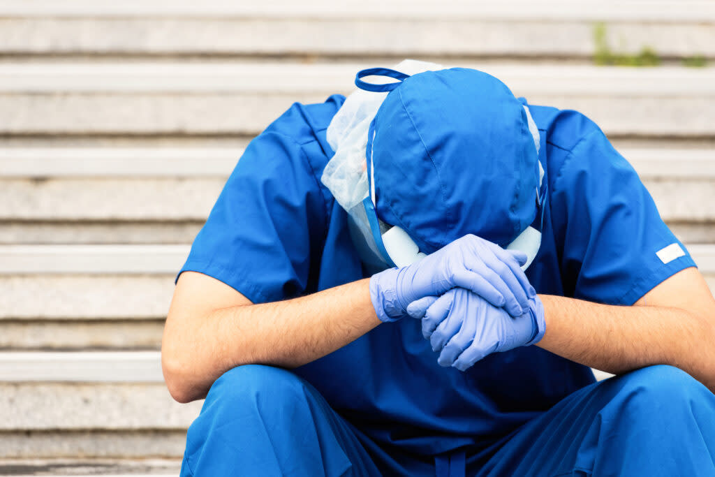 an overworked male nurse sits outside hospital