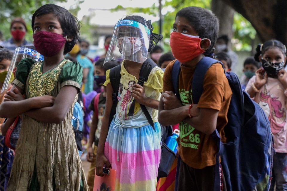 Colorfully clothed children wear masks and carry backpacks