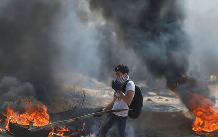 A Palestinian passes burning tires during clashes with Israeli troops at a protest demanding the right to return to their homeland, at the Israel-Gaza border east of Gaza City April 6, 2018. REUTERS/Mohammed Salem