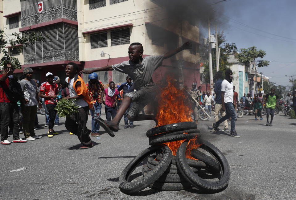 A child jumps over a burning barricade during anti-government protests in Port-au-Prince, Haiti, Friday, Oct. 11, 2019. Protesters burned tires and spilled oil on streets in parts of Haiti's capital as they renewed their call for the resignation of President Jovenel Moïse just hours after a journalist was shot to death. (AP Photo/Rebecca Blackwell)
