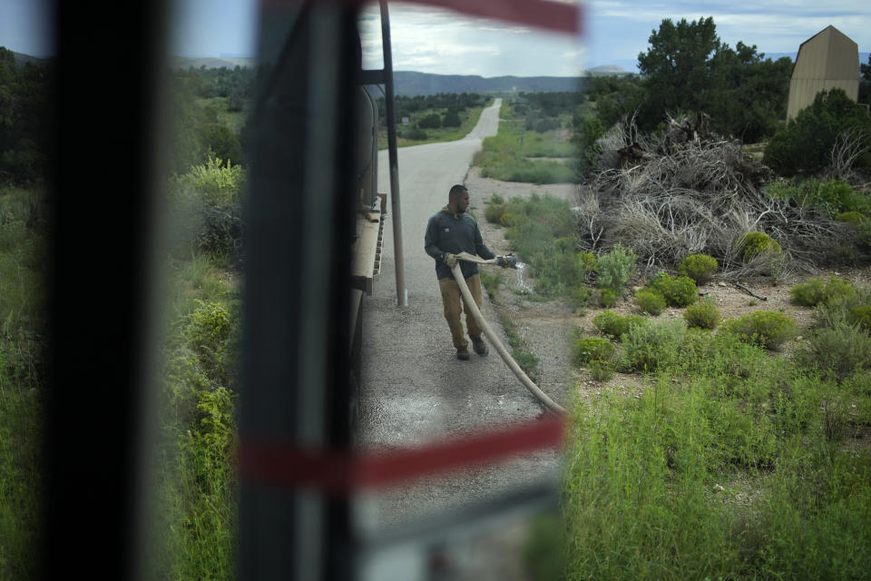 Garnett Querta attaches a water hose to his truck on the Hualapai reservation Monday, Aug. 15, 2022, in Peach Springs, Ariz. Tape helps keep the rearview mirror from falling off as he navigates dirt roads while hauling water. (AP Photo/John Locher)