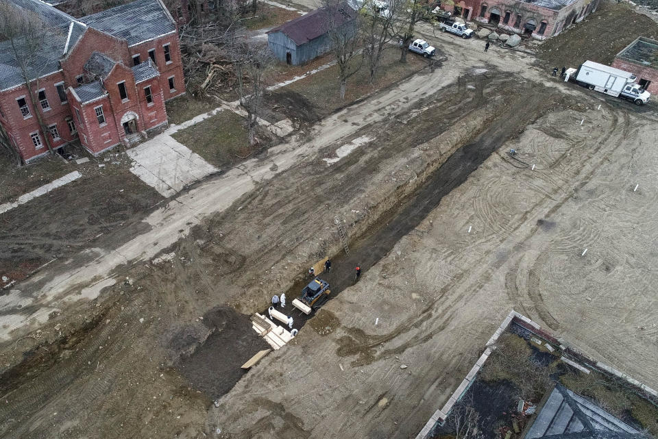 Workers wearing personal protective equipment bury bodies in a trench on Hart Island, Thursday, April 9, 2020, in the Bronx borough of New York. On Thursday, New York City’s medical examiner confirmed that the city has shortened the amount of time it will hold on to remains to 14 days from 30 days before they will be transferred for temporary internment at a City Cemetery. Earlier in the week, Mayor Bill DeBlasio said that officials have explored the possibility of temporary burials on Hart Island, a strip of land in Long Island Sound that has long served as the city’s potter’s field. (AP Photo/John Minchillo)