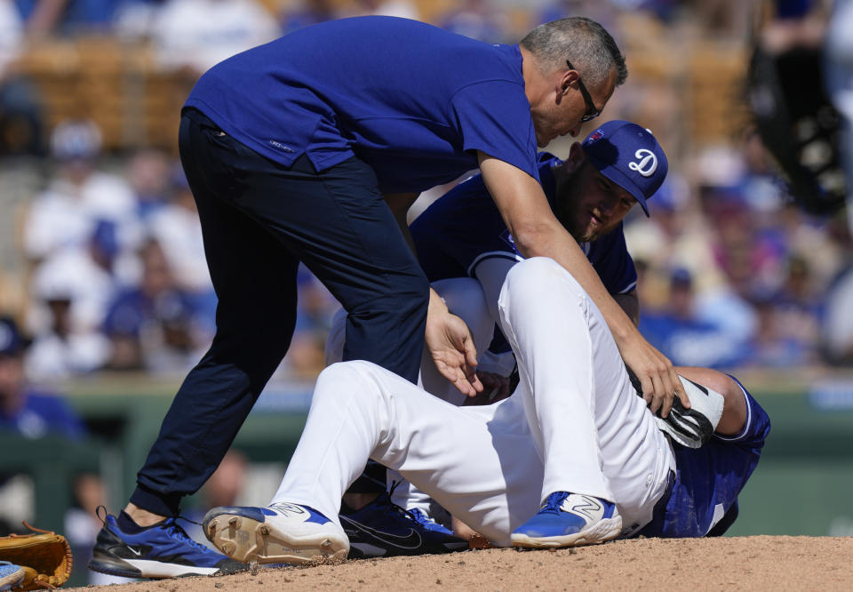Los Angeles Dodgers relief pitcher Blake Treinen, bottom, is tended to by teammate Max Muncy, center, and a trainer, top, after being hit by a ball in the fifth inning of a spring training baseball game against the Texas Rangers, Saturday, March 9, 2024, in Phoenix. Treinen left the game with a right rib contusion. (AP Photo/Carolyn Kaster)