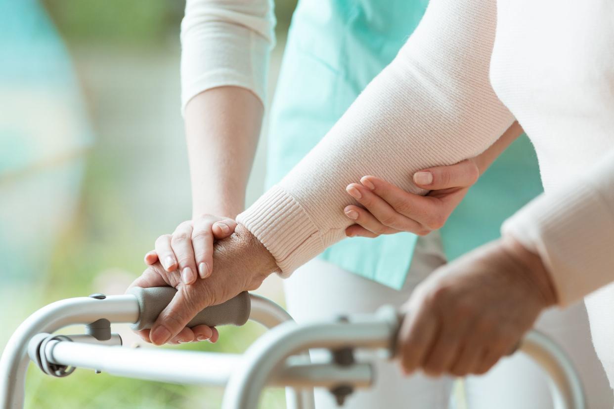 nurse helps parkinson's patient maintain hands on walker