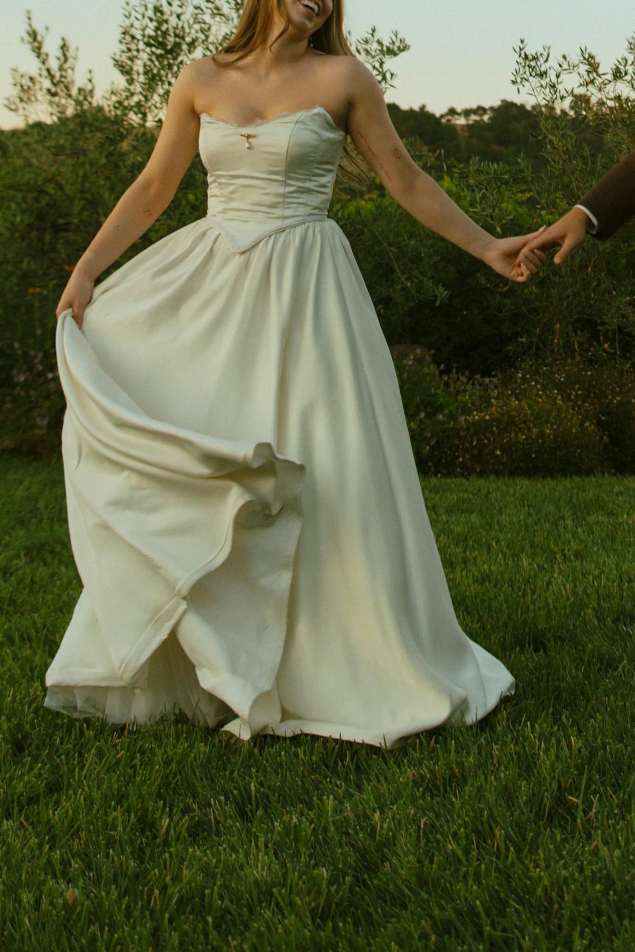 A close-up shot of a bride's wedding dress with a pearl in the center of the bodice as she stands in a field.