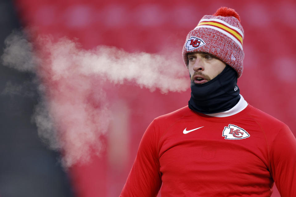 Harrison Butker wearing a Kansas City Chiefs beanie exhales visible breath in cold weather while on the field