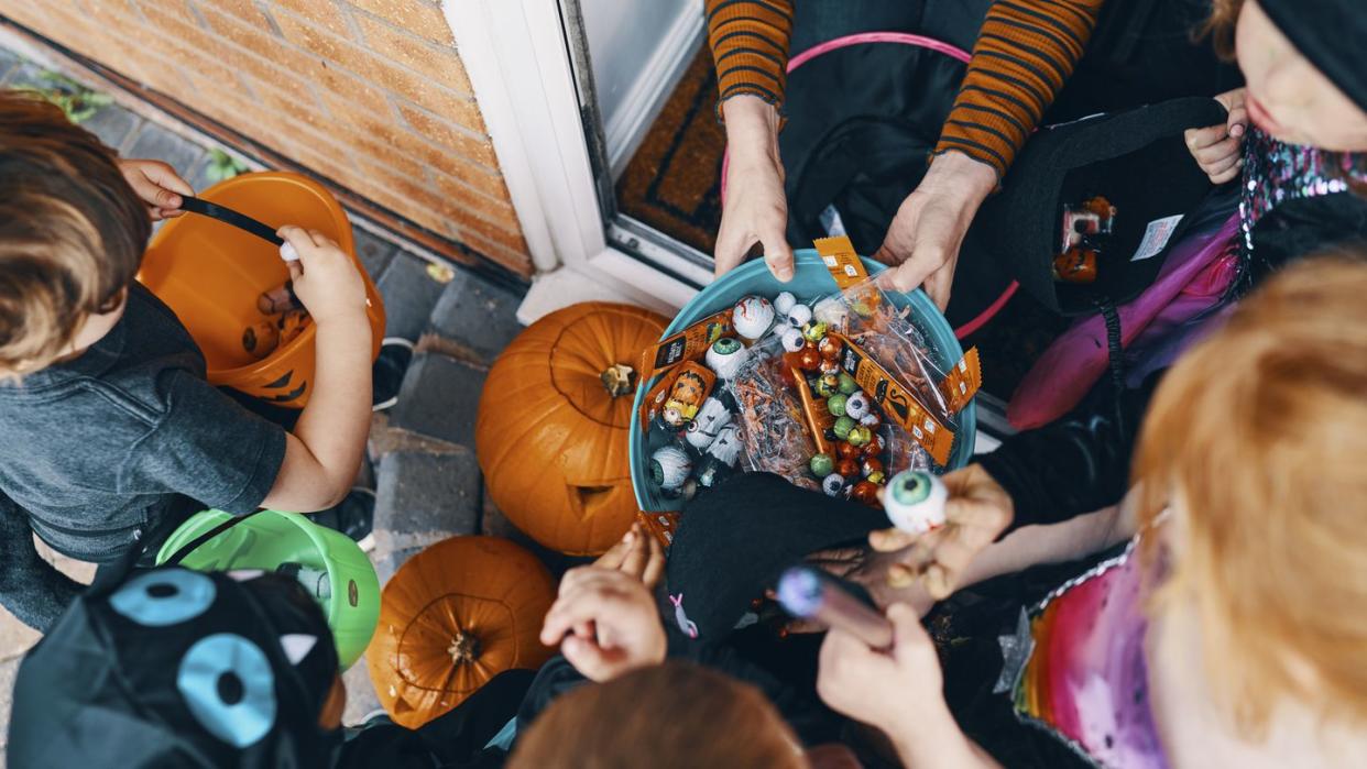 overhead view of a group of children at a front door taking sweets from a bowl at halloween