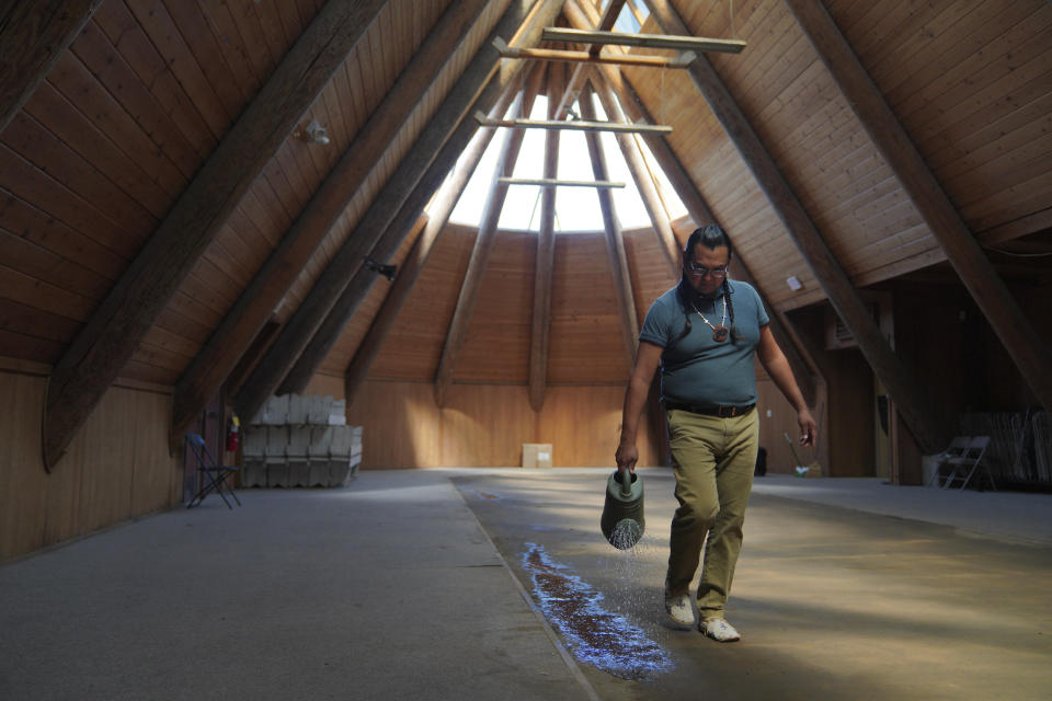 Bronsco Jim Jr., mid-Columbia River chief, cleans the longhouse altar, a rectangle of Earth, with water before a ceremonial meal at the Celilo Village longhouse on Sunday, June 19, 2022, in Celilo Village, Ore. The tribe's first foods are placed on the table in seasonal order before the meal begins. (AP Photo/Jessie Wardarski)