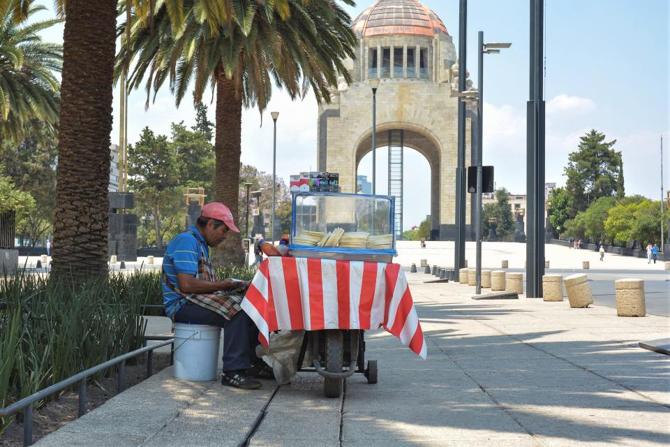 MEXICO CITY, MEXICO - APRIL 6: Street seller reed the newspapper near of 'Monumento a la Revolucion' during a quiet afternoon in the historic center due to the #SanaDistancia campaign, which asks the public to respect social distancing and keep a minimum of 1.5 meters apart as the government attempts to prevent the spread of coronavirus (COVID-19) in the city, on April 6, 2020 in Mexico City, Mexico. Health Emergency was declared by National Government and Non-essential activities have been suspended nationwide until April 30. The Coronavirus (COVID-19) pandemic has spread to many countries across the world, claiming over 70,000 lives and infecting over a million more. (Photo by Medios y Media/Getty Images)