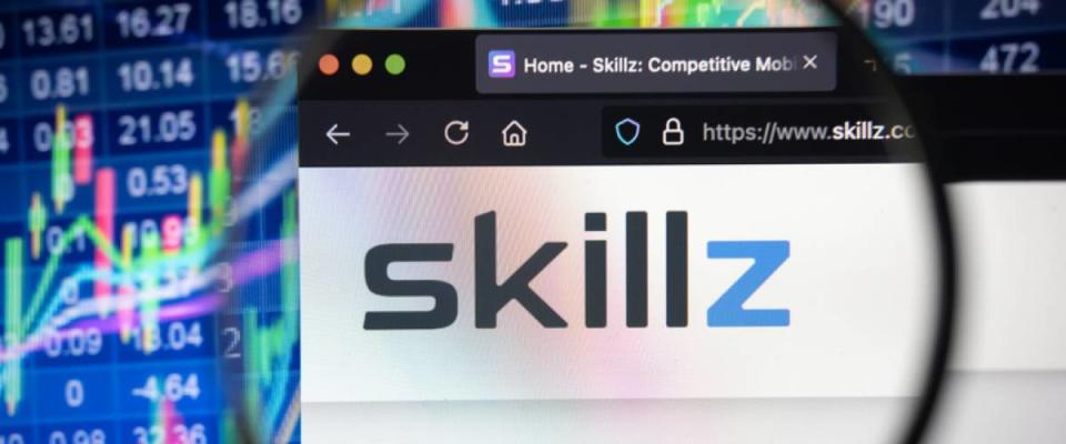 Skillz company logo on a website with blurry stock market developments in the background, seen on a computer screen through a magnifying glass.