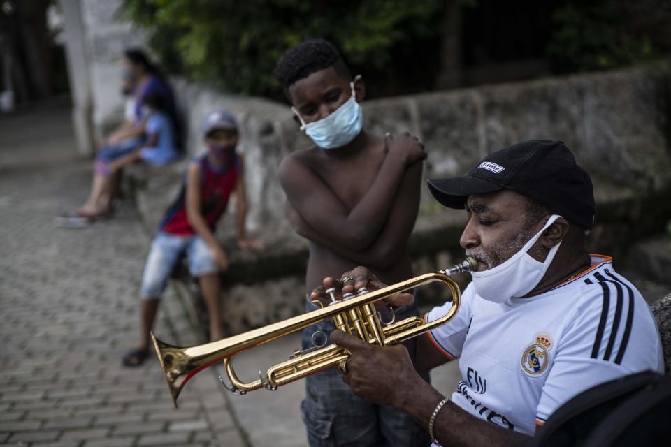 Con una máscara facial en medio de la pandemia del nuevo coronavirus, un niño observa las prácticas del trompetista Carlos Sánchez en preparación para la llegada de turistas en La Habana Vieja, Cuba, el martes 27 de octubre de 2020. (AP Foto/Ramón Espinosa)