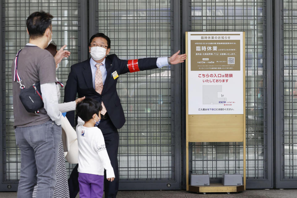 An usher briefs visitors at an entrance of a department store which is open partially, in Tokyo Sunday, April 25, 2021. Japan’s department stores, bars and theaters shuttered Sunday, as the government “state of emergency” over the coronavirus pandemic kicked in amid growing worries about a surge in infections. (Hiroko Harima/Kyodo News via AP)