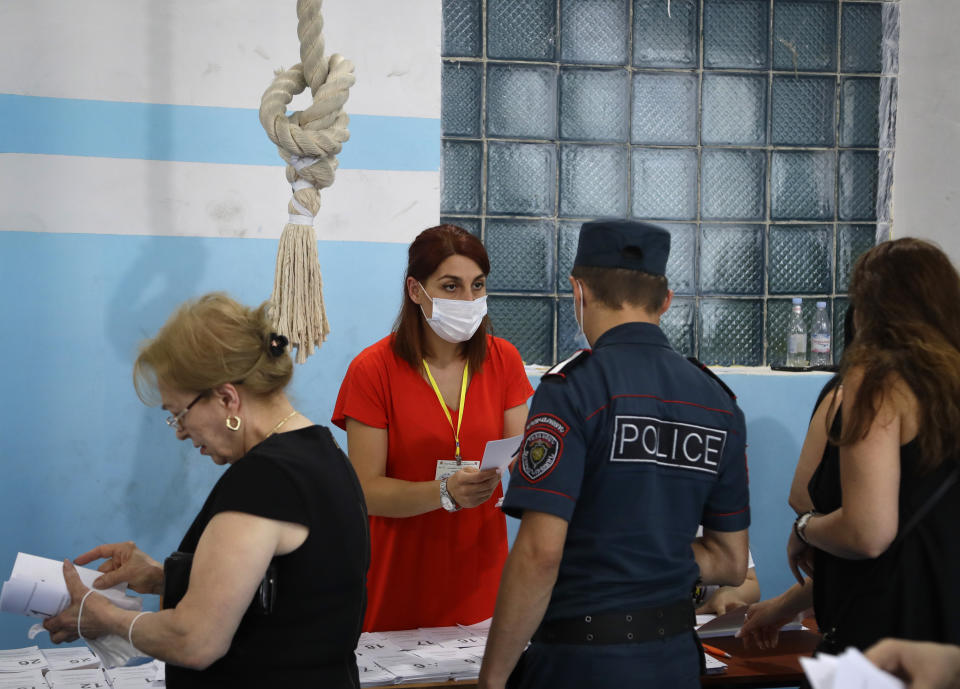 Voters receive their ballot papers at a polling station during a parliamentary election in Yerevan, Armenia, Sunday, June 20, 2021. Armenians are voting in a national election after months of tensions over last year's defeat in fighting against Azerbaijan over the separatist region of Nagorno-Karabakh. (AP Photo/Sergei Grits)