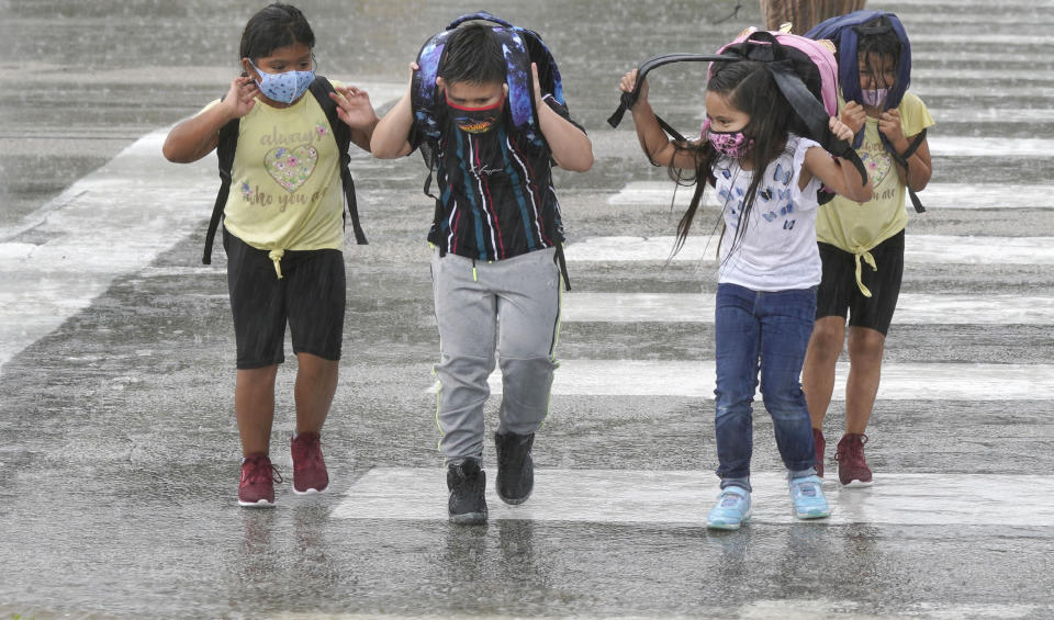 Elementary school children wear masks as they make their way across the street after school let out during a rain storm in Richardson, Texas, Wednesday, Sept. 9, 2020. Many schools across Texas resumed face to face classes this week. (AP Photo/LM Otero)
