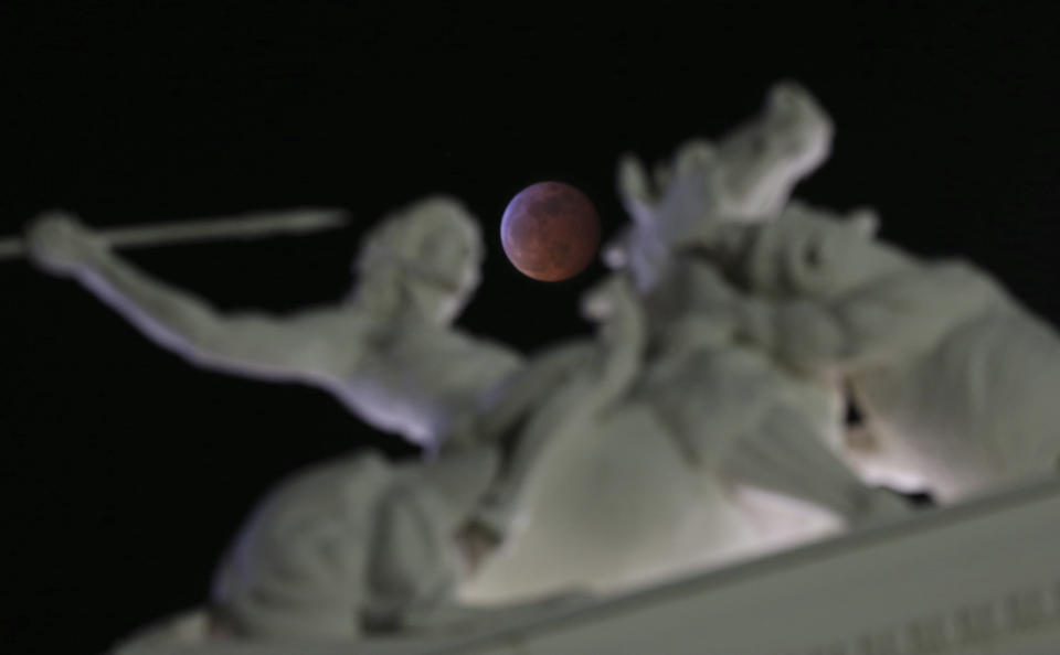 The moon is framed in a statue on the state Capitol during a total lunar eclipse Sunday, Jan. 20, 2019, in Sacramento, Calif. The entire eclipse will exceed three hours. Totality-when the moon's completely bathed in the Earth's shadow-will last an hour. Expect the eclipsed or blood moon, to turn red from the sunlight scattering off Earth's atmosphere. (AP Photo/Rich Pedroncelli)