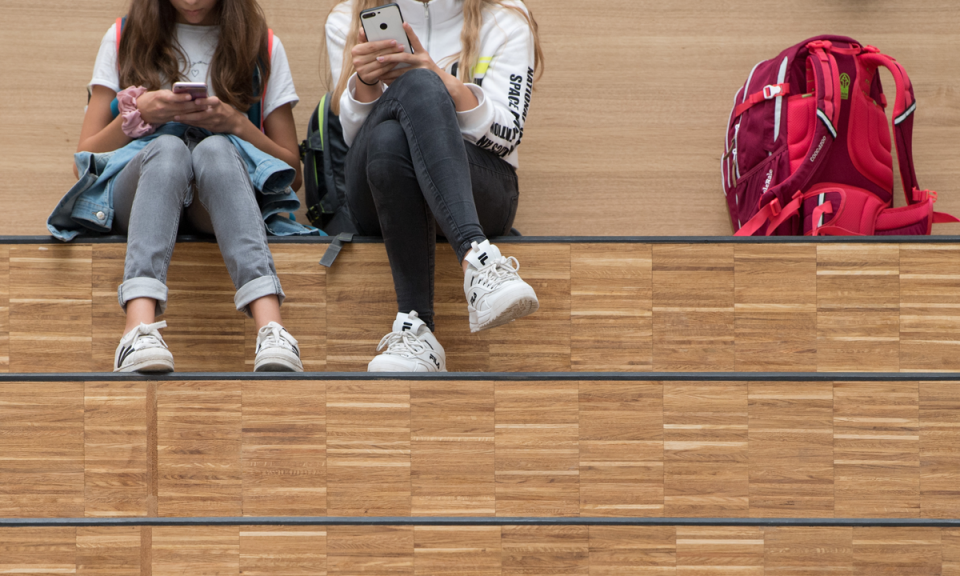 Two students sitting on bleachers using their phones