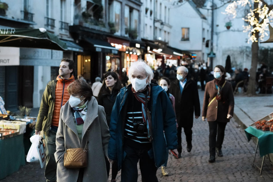 Pedestrians, some wearing protective face masks to prevent the spread of the COVID-19, walk in street market, in Paris, France, Friday, Dec. 31, 2021. Paris region health authorities have instructed hospitals to cancel more non-urgent medical procedures to free up intensive-care beds for the growing influx of people gravely sick with COVID-19. (AP Photo/Thibault Camus)