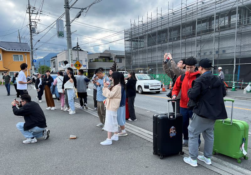 Tourists try to take photos of Mount Fuji appearing over a convenience store from the parking spot of the store in Fujikawaguchiko