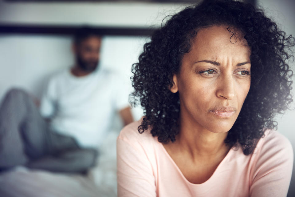 Two people, one in the foreground looking concerned and another sitting in soft focus in the background