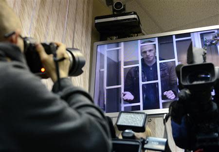 Photographer Denis Sinyakov, one of the 30 people detained after a Greenpeace protest at the Prirazlomnaya platform who is currently held at a pretrial detention centre, is seen on a screen installed inside a court building during a court session in Murmansk, October 8, 2013. REUTERS/Stringer