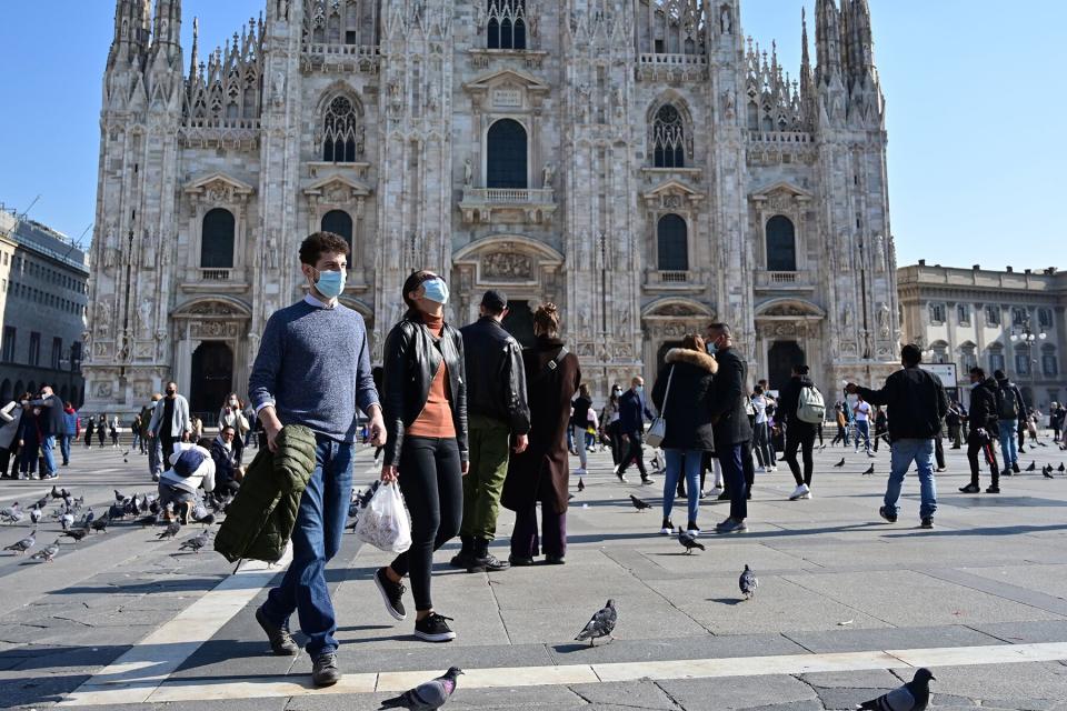 People wearing protective masks walk across the Piazza del Duomo in Milan