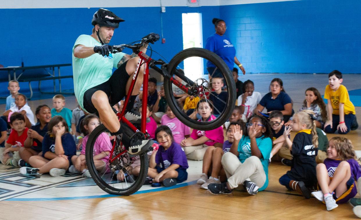 Jeff Lenosky, a professional mountain bicyclist, rides a wheelie around a group of children in an after-school program at the Boys and Girls Clubs of Polk County's James J. Musso Unit in Lakeland on Wednesday afternoon. Lenosky was there as part of a bike giveway organized by Can'd Aid and the Yasso Game On! Foundation.